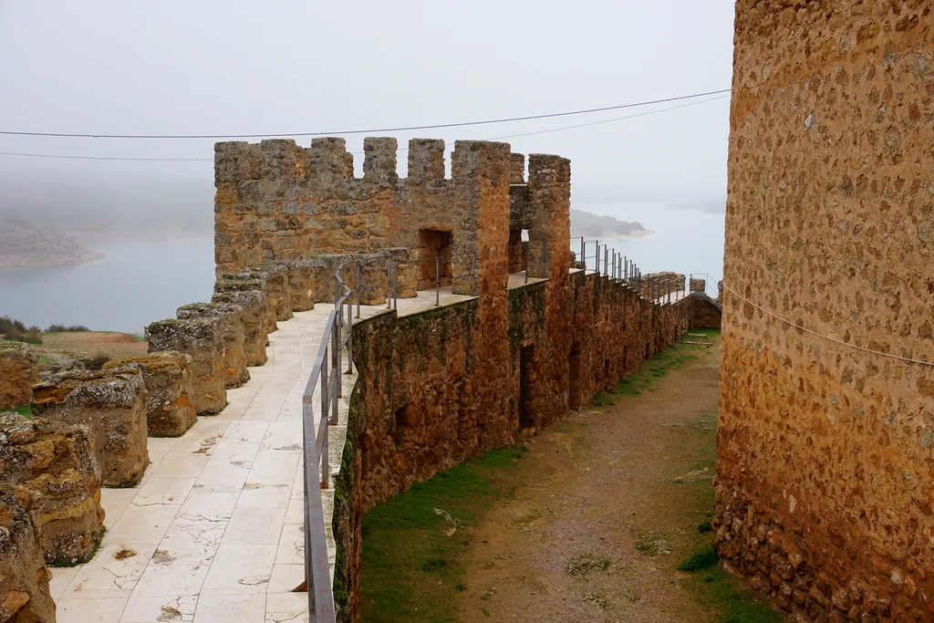 Camino de ronda sobre las murallas almenadas del castillo de Peñarroya con el embalse al fondo