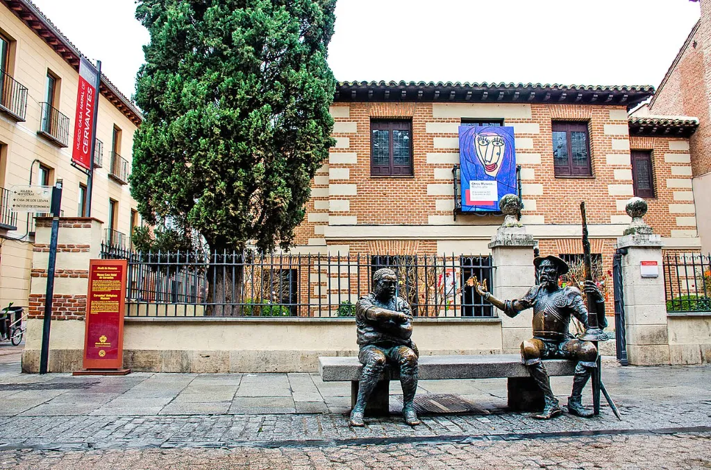 Fachada del Museo Casa Natal de Cervantes con las estatuas de don Quijote y Sancho Panza sentados en un banco