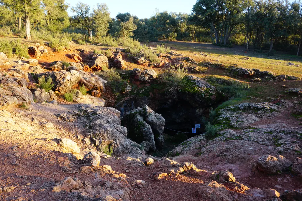 Boca de la Cueva de Montesinos, una sima entre rocas calizas rojizas rodeada de encinas