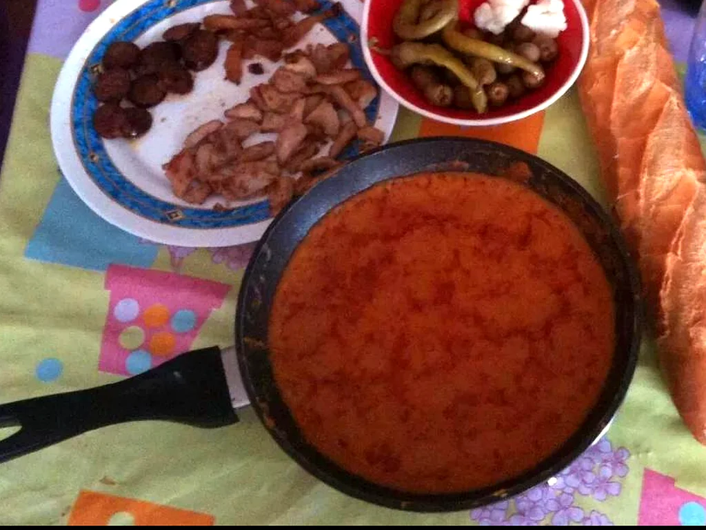 Sartén de gachas manchegas en la mesa, con torreznos, chorizo, guindillas y pan