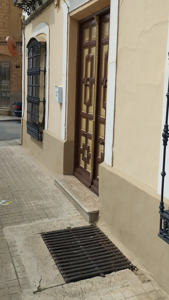 Lumbrera de una cueva-bodega con rejilla en la acera junto a la fachada de una casa de Tomelloso