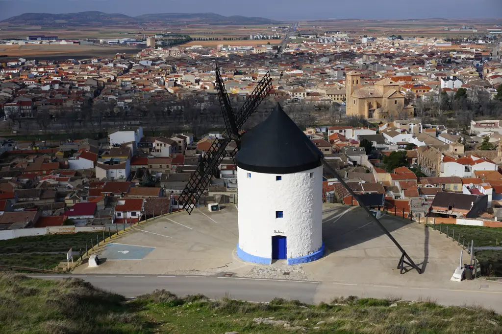 Molino de viento blanco con zócalo azul y el pueblo de Consuegra a sus pies