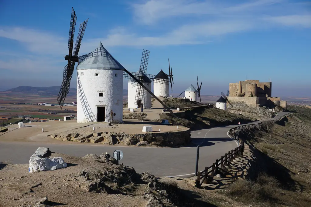 Molino blanco en primer plano con otros molinos y el castillo de La Muela al fondo, en el Cerro Calderico de Consuegra