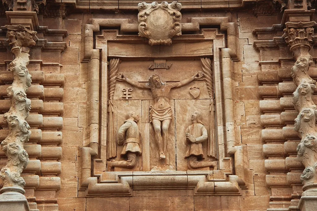 Relieve en piedra de Cristo crucificado entre dos figuras en la portada de la iglesia del Cristo del Valle