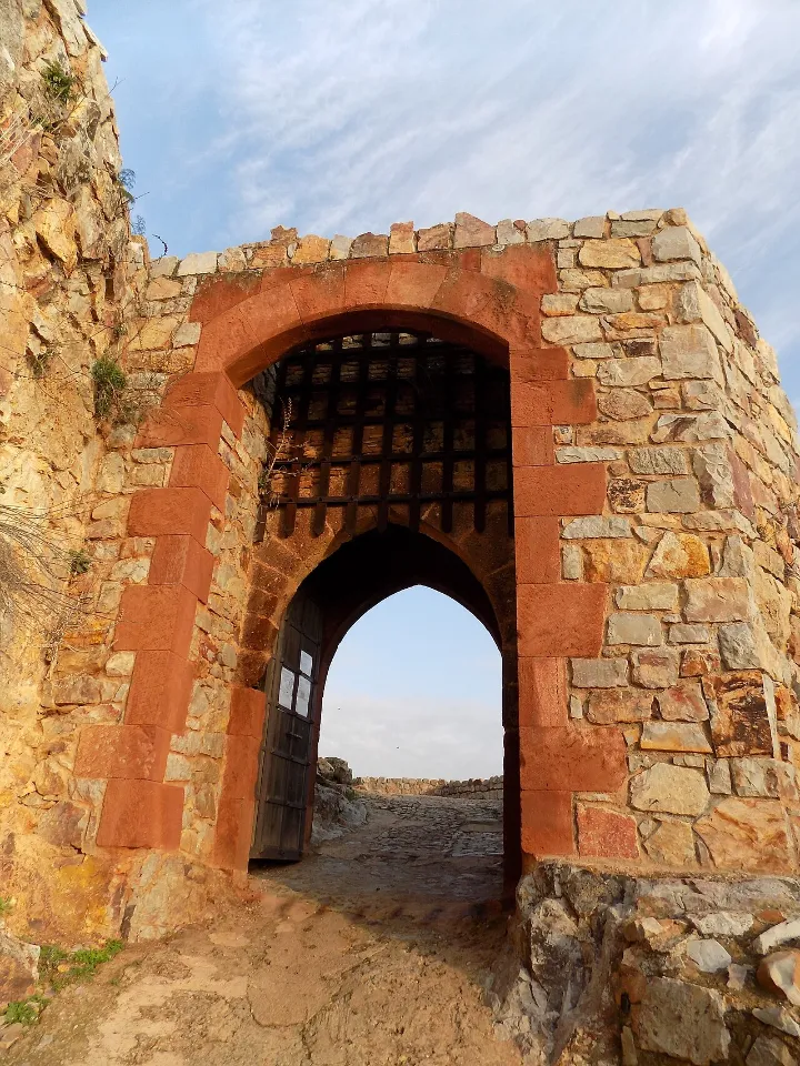 Puerta de acceso con arco de piedra volcánica rojiza y rastrillo en el castillo de Calatrava la Nueva